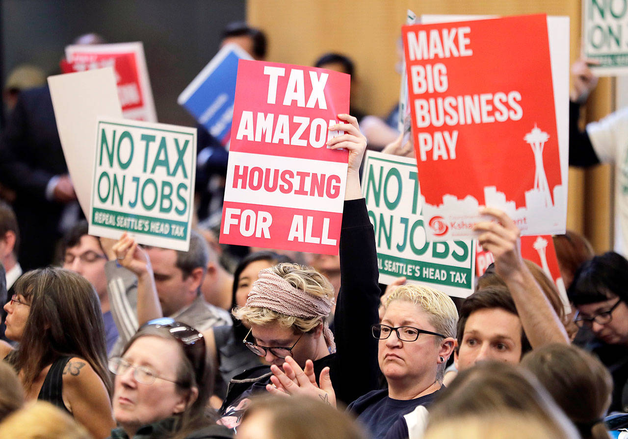 People attending a Seattle City Council meeting on Tuesday hold signs as the listen to public comment before the council voted to repeal of a tax on large companies intended to combat a growing homelessness crisis. (AP Photo/Ted S. Warren)