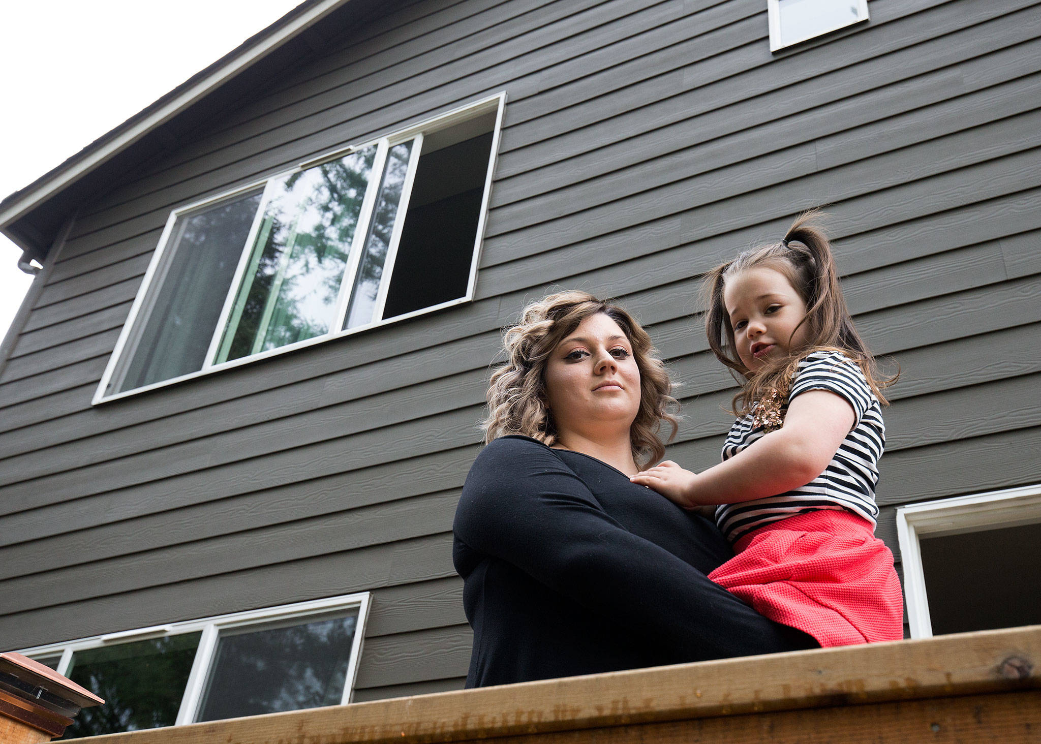 Kate Hitter holds her youngest daughter, Scarlett, under a third-story window at their Lake Stevens home on May 1 in Lake Stevens. While the family was moving in in 2017, Scarlett fell through a screened window and landed on the concrete patio 30 feet below. (Andy Bronson / The Herald)