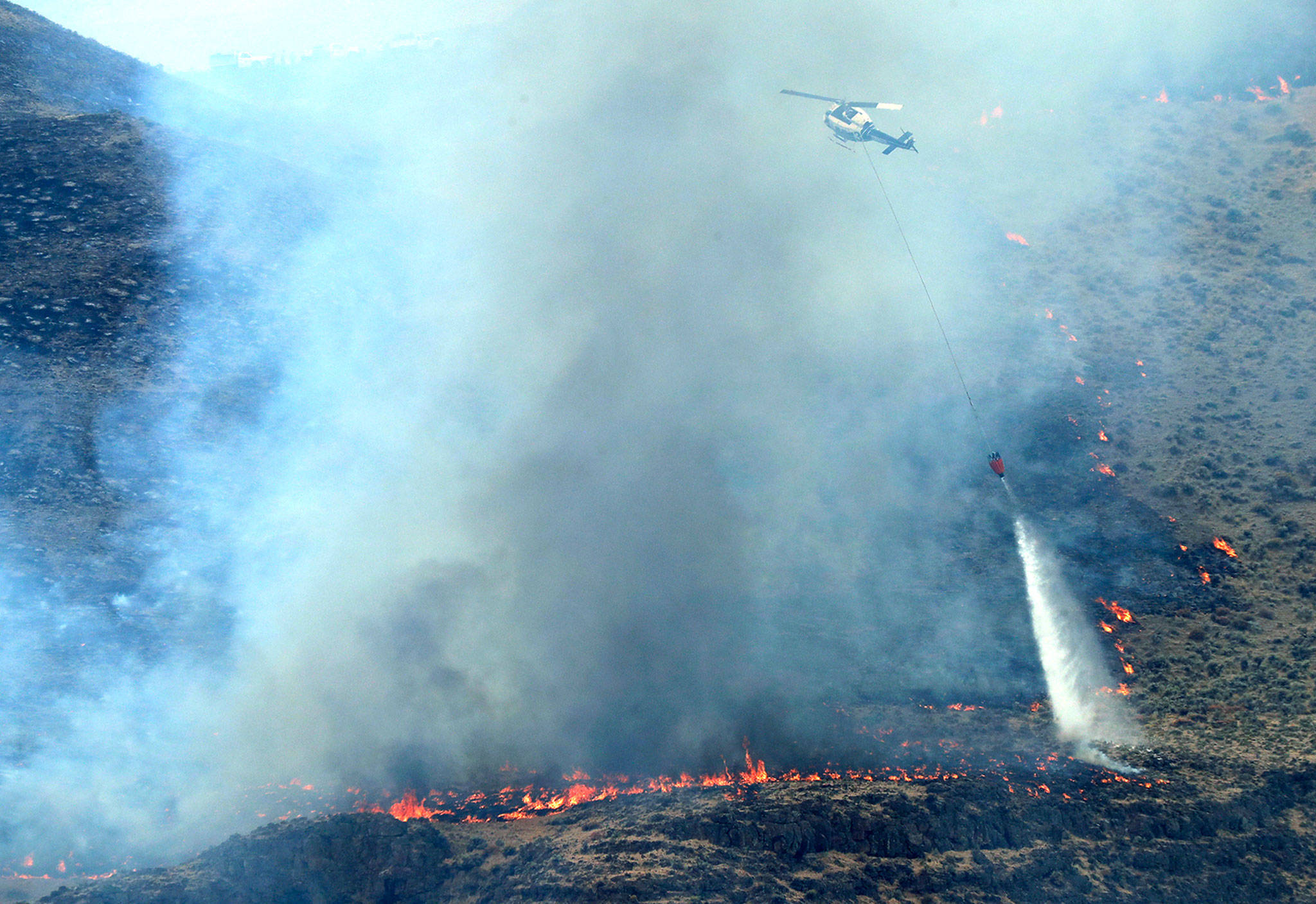 A helicopter uses a bucket to drop water on the Milepost 22 wildfire Thursday near Vantage. (AP Photo/Ted S. Warren)