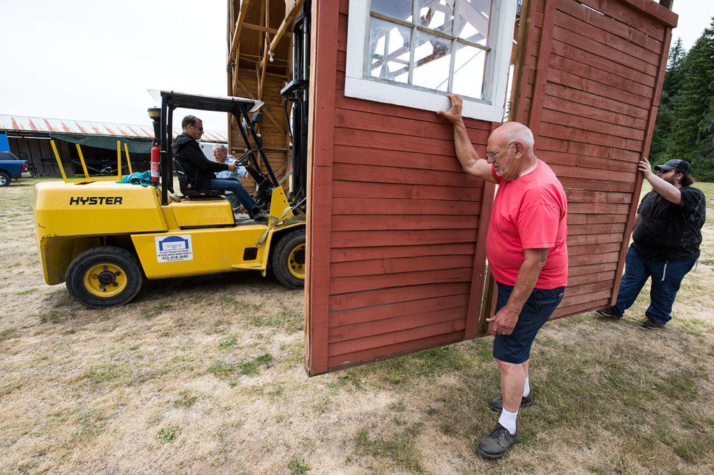 Volunteers, Bruce Angell, on forklift, Ralph Frazier, Pat Connelly, in red, and Roland Shaw move a section of the red barn to its new position at the Arlington Airport, in preparation for the Arlington Fly-In. The barn is the centerpiece of a historic airplane exhibit during the airshow event. (Andy Bronson / The Herald)
