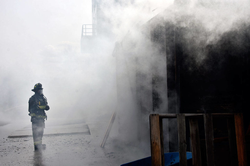 A firefighter recruit watches a burning shipping container that serves as a mock apartment during live fire training at Snohomish County’s first fire academy on April 19. (Caleb Hutton / The Herald)
