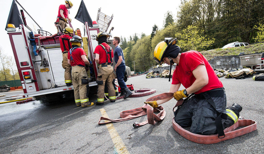 After a day of learning to fight fires, Everett firefighter recruit Chau Nguyen flakes a hose as other recruits load the hoses onto a fire truck at a training facility April 19 in Snohomish. (Andy Bronson / The Herald)
