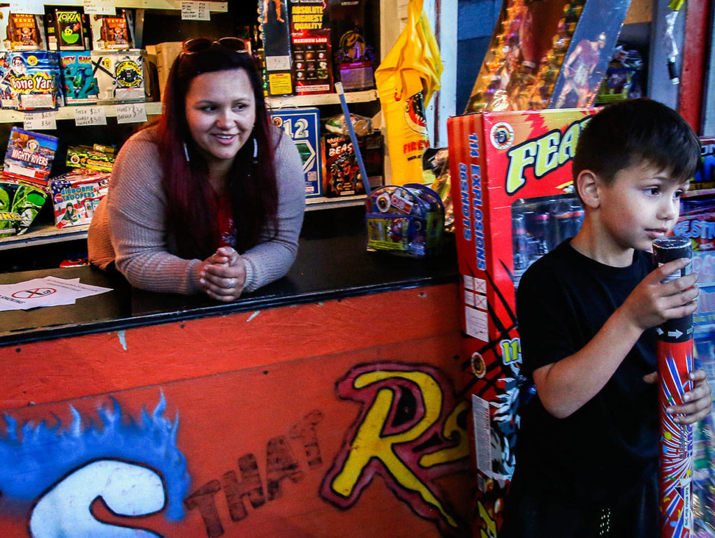 Eliza Davis, 37, smiles as she watches her 6-year-old nephew, Micah Thornberry, take a confetti blaster she gave him to pop open with another youngster outside her stand, Fireworks that Rock. At 10, Davis began selling fireworks with her parents. She now serves on the tribes’ Boom City Committee. (Dan Bates / The Herald)
