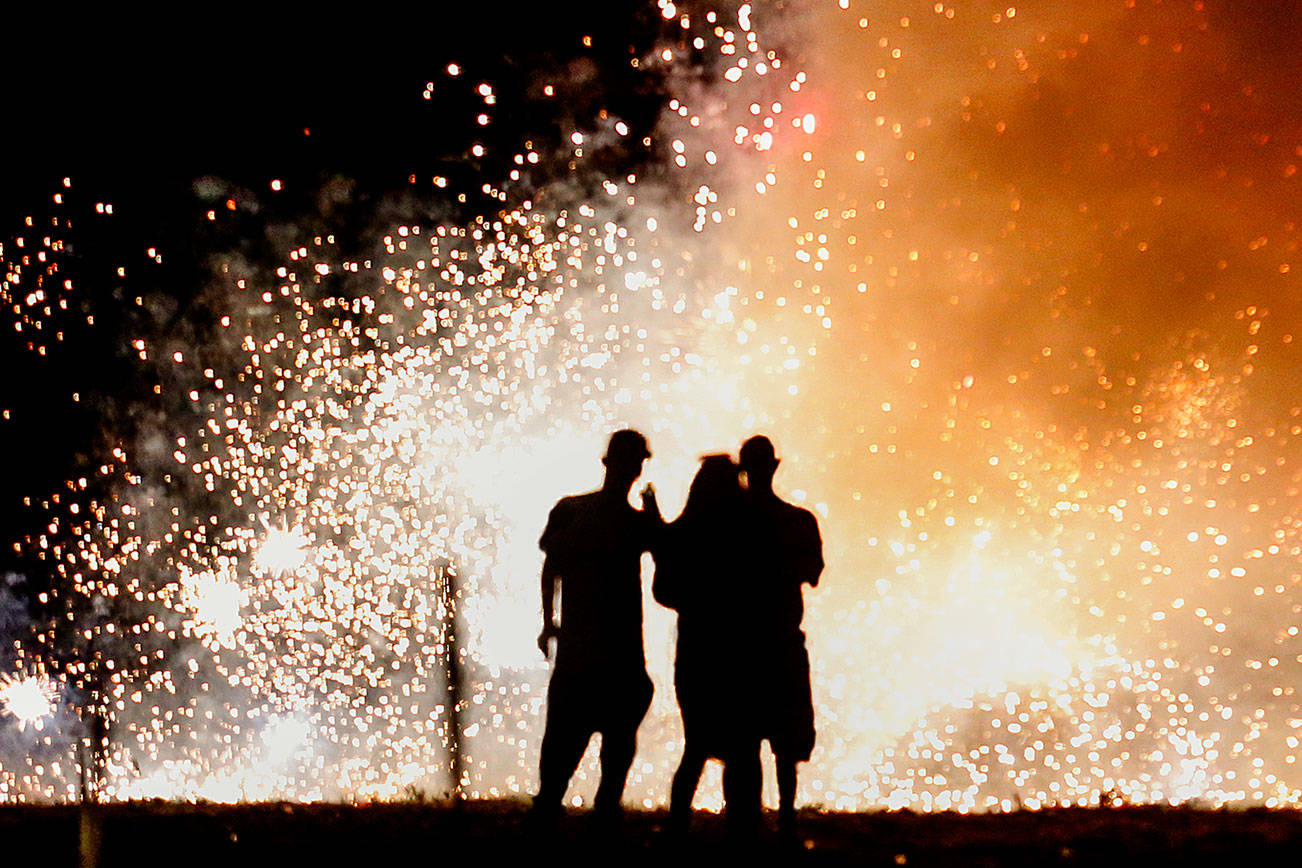 A trio in the lighting area at Boom City watches a shower of white-hot sparks from several fountains set off Tuesday just as darkness falls. (Dan Bates / The Herald)