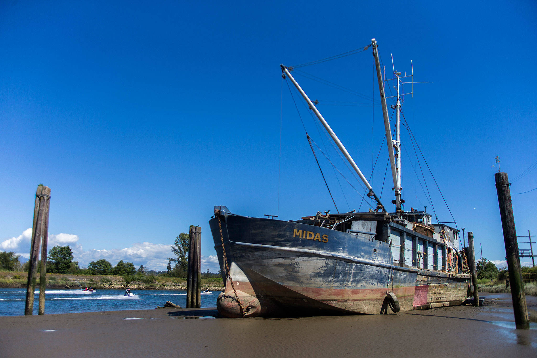 People on jet skis and boats drive past the Hannah Marie on Tuesday in Everett. The boat formerly called the Midas was run aground on the banks of the Snohomish River in Everett. (Olivia Vanni / The Herald)