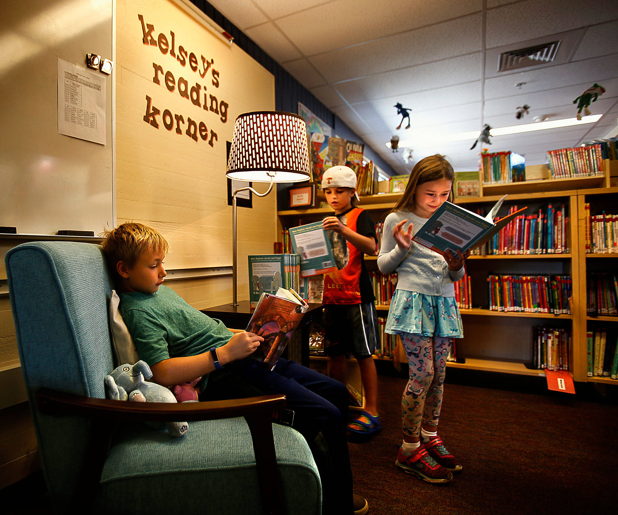 Darren Howe, 9, sits in a comfy chair reading “Harry Potter and the Sorcerer’s Stone” while his cousin, Naven Collins, 7, (center) stands delighting in a “Elephant and Piggie” book, which is from the same collection that Mya Illingworth, 6, (back middle) is looking through in Kelsey’s reading Korner at Sunnycrest Elementary School Wednesday. With the addition of Kelsey’s Korner, featuring the kind of books she encouraged her kids to read, the school now has two places that honor Kelsey Osborne, a much loved teacher who died in June. (Dan Bates / The Herald)