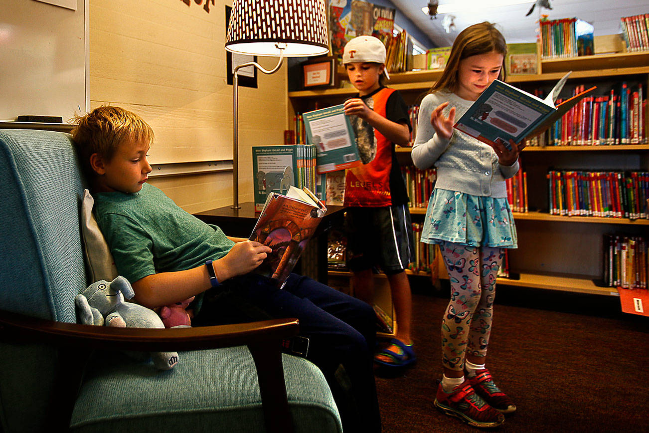 Darren Howe, 9, sits in a comfy chair reading Harry Potter and the Sorcerer’s Stone while his cousin, Naven Collins, 7, (center) stands delighting in a Elephant and Piggie book, which is from the same collection that Mya Illingworth, 6, (back middle) is looking through in Kelsey’s reading Korner at Sunnycrest Elementary School Wednesday. With the addition of “Kelsey’s Korner,” featuring the kind of books she encouraged her kids to read, the school now has two places that honor Kelsey Osborne, a much loved teacher who died in June. (Dan Bates / The Herald)