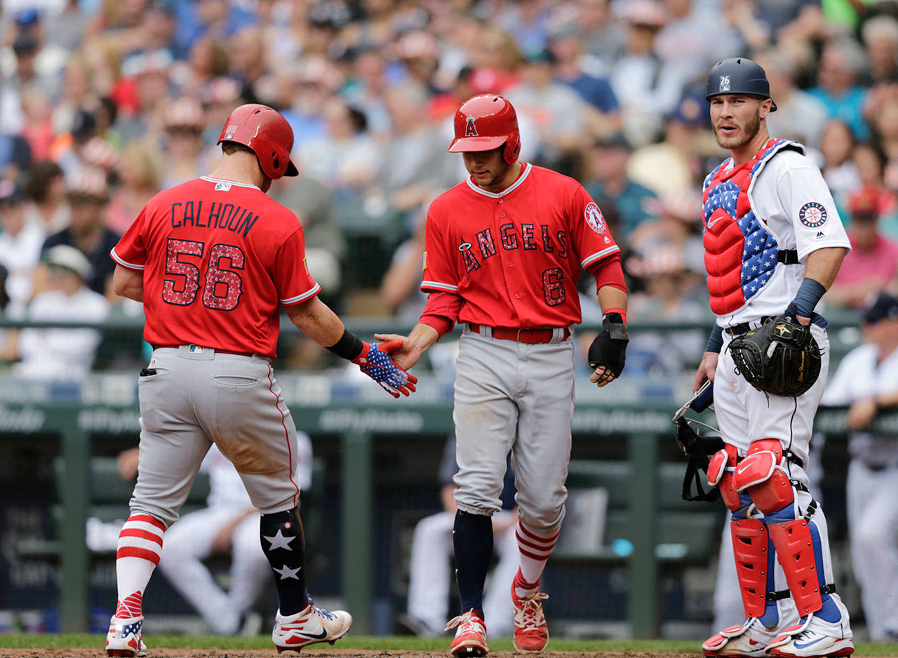 The Angels’ Kole Calhoun is greeted by David Fletcher after hitting a home run, while Mariners catcher Chris Herrmann looks away during the sixth inning on July 4, 2018, in Seattle. (AP Photo/John Froschauer)