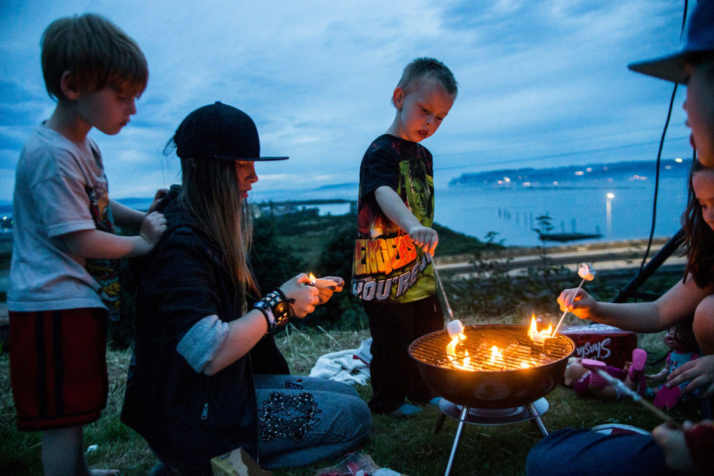 Junior Holmes (right) roasts a marshmallow while Sirus True (left), 5, watches Alyssia Hosmer, 14, light paper for the grill at Legion Memorial Park on Wednesday in Everett. (Olivia Vanni / The Herald) 
