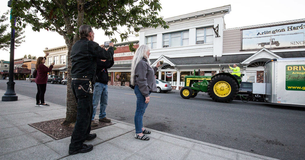 Family members take photos and wave as Jeff Newell cruises through downtown Arlington on his John Deere tractor, en route to Prudhoe Bay, Alaska, on July 11. (Andy Bronson / The Herald)

