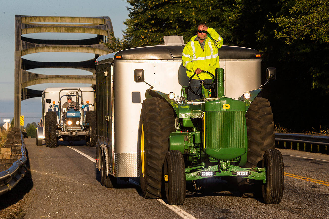 Jeff Newell blocks the early morning sun from his eyes as he cruises down Highway 530, at a easy 16 miles per hour, on his John Deere tractor on Wednesday, July 11, 2018 in Arlington, Wa. Ron Wachholtz follows behind as the two raise money while driving their tractors to Prudhoe Bay, AK. They are raising money for the American Diabetes Association. (Andy Bronson / The Herald)
