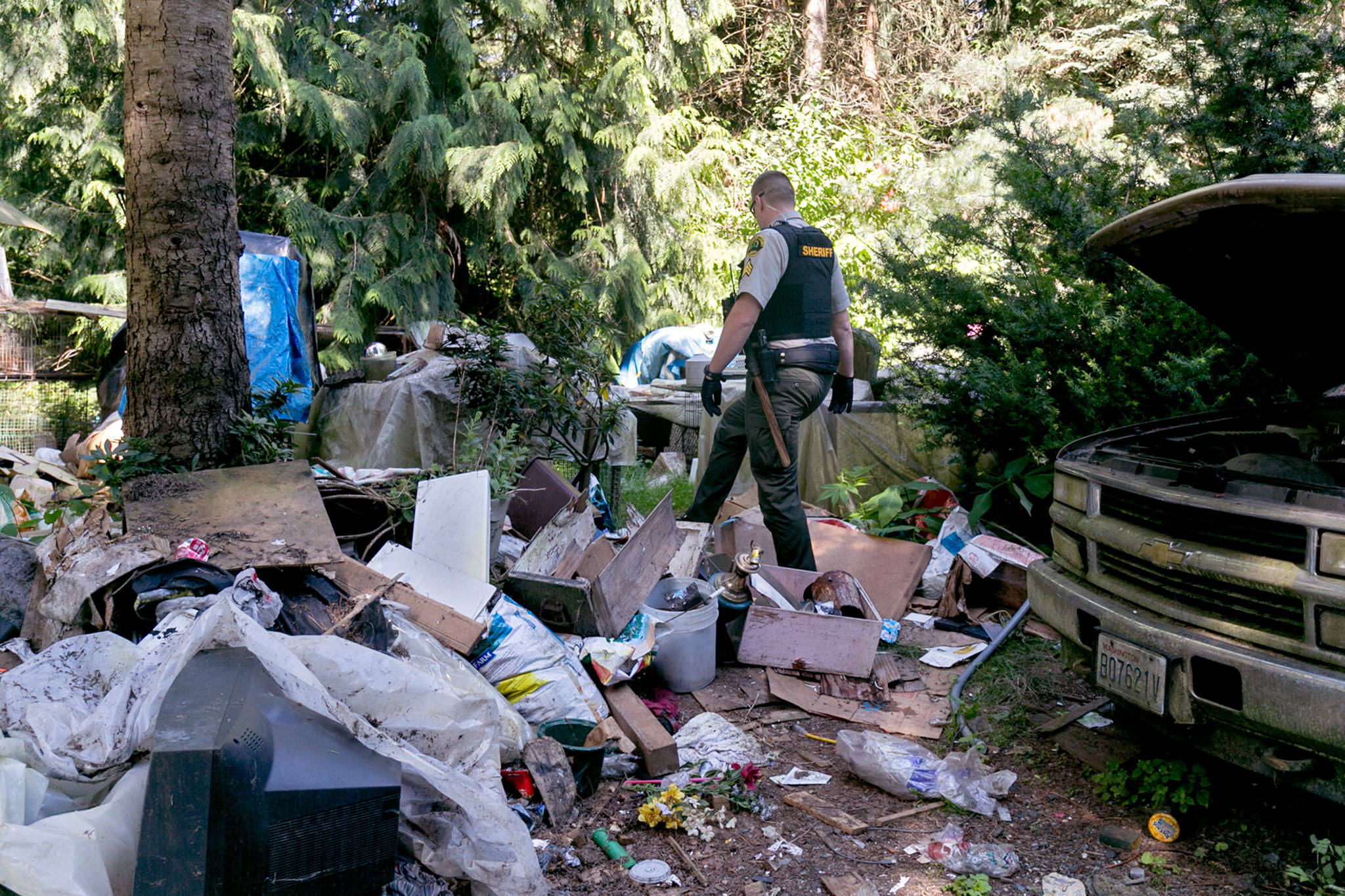 Snohomish County sheriff’s Sgt. Alex Scott walks through detritus of a nuisance house near Woodinville on July 11. (Kevin Clark / The Herald)