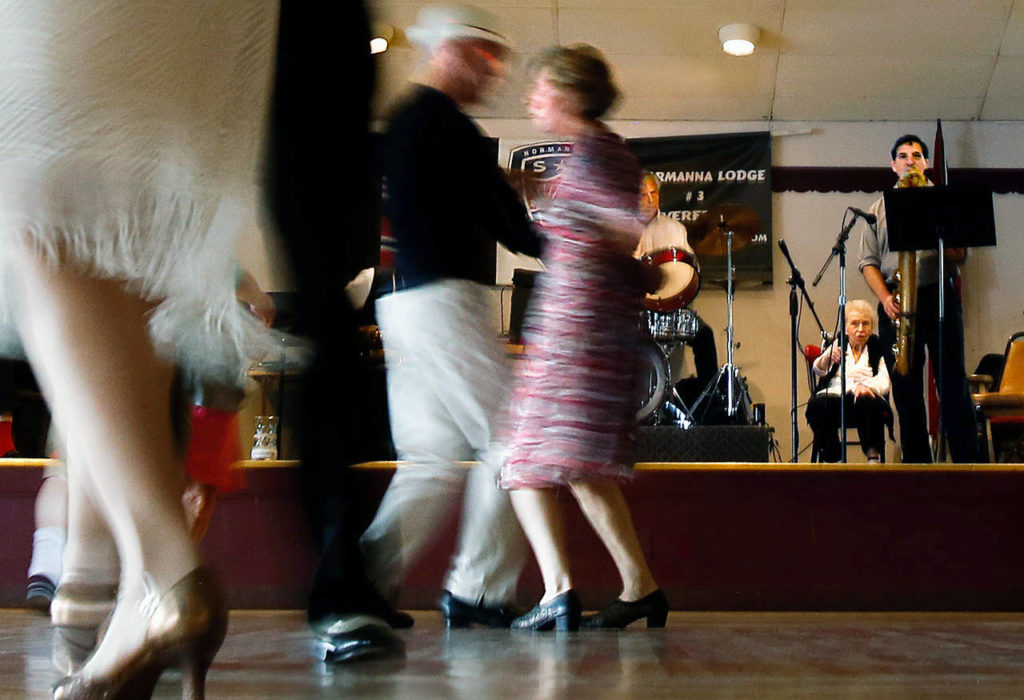 As dancers Patrick Maguire, 81, and Joyce Laux, 79, go past the stage in a blur, Barry (on drums), Purvis and baritone sax player Nathaniel Paul Schleimer belt out dance music. (Dan Bates / The Herald)
