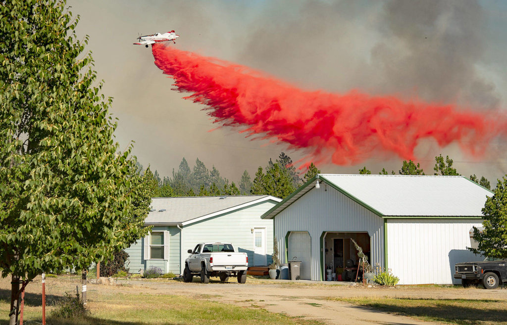 A firefighting aircraft makes a retardant drop on a wildfire approaching a house Tuesday in Spokane. (Colin Mulvany / The Spokesman-Review)

