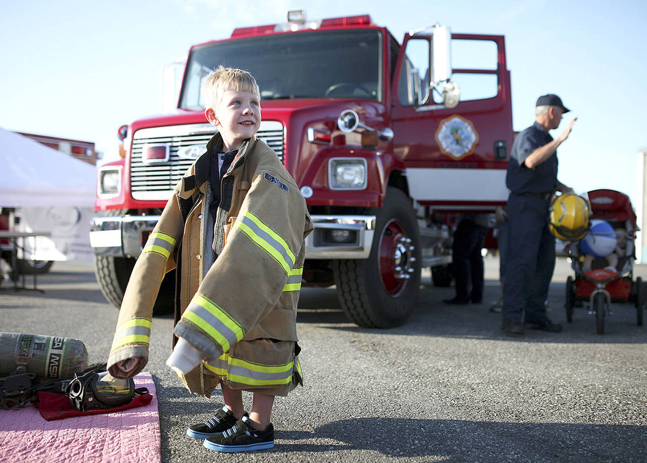 Donning a firefighting jacket, Wesson Fischer, then 4, smiles as he stands in front of a Camano Island fire engine during Stanwood’s National Night Out in 2014. This year’s event is set for Aug. 7. (Herald file)