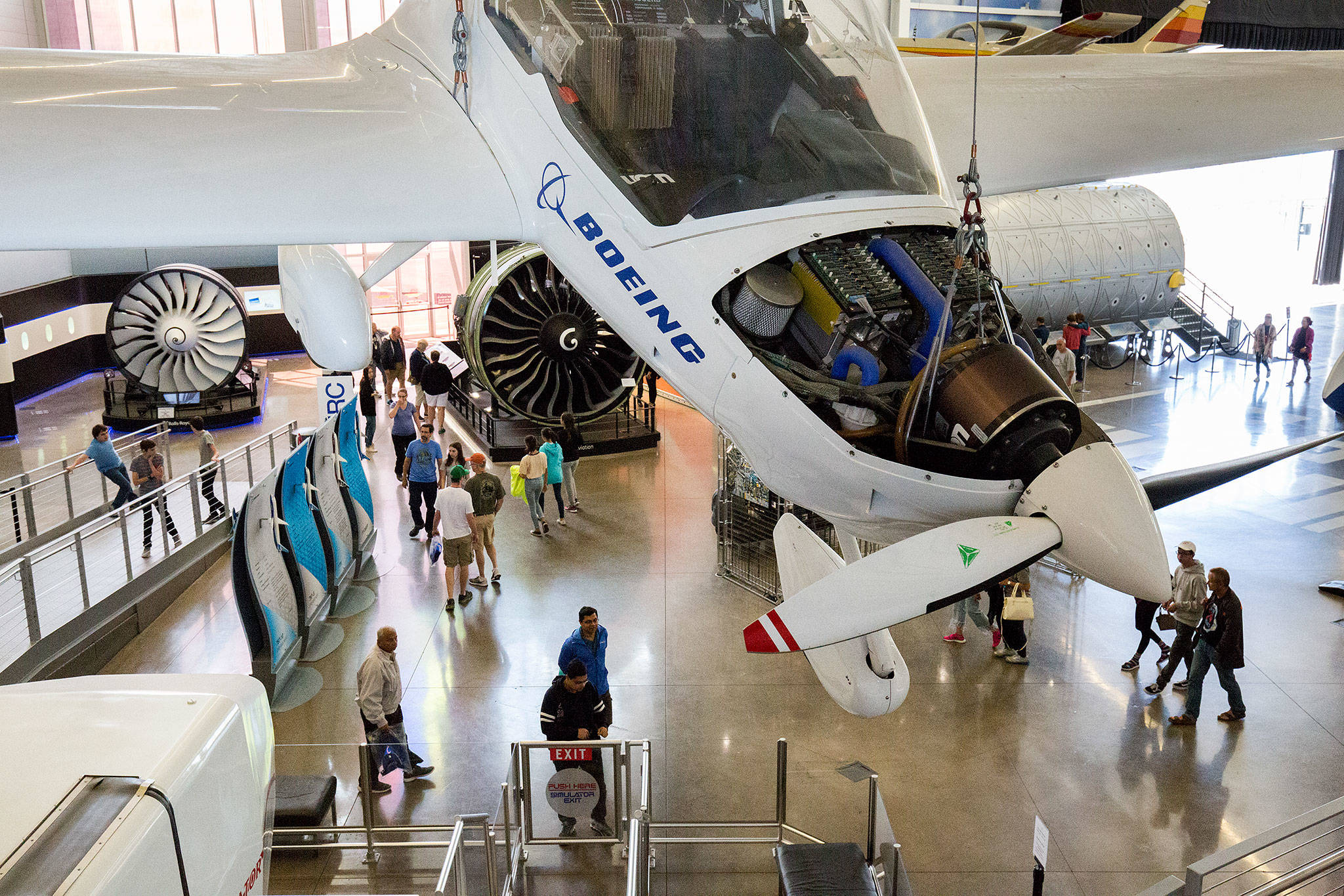 An experimental Boeing plane hangs above visitors looking at engines and planes on display at the Future of Flight on Friday in Mukilteo. The Boeing Co. plans this year to operate the Future of Flight Aviation Center. (Andy Bronson / The Herald)