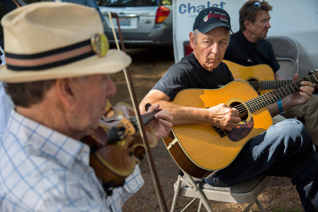 Fred Holt, center, looks at Gene Silberberg, right, during a practice session in the camping area during the Darrington Bluegrass Festival on Saturday, July 21, 2018 in Darrington, Wa. (Olivia Vanni / The Herald)
