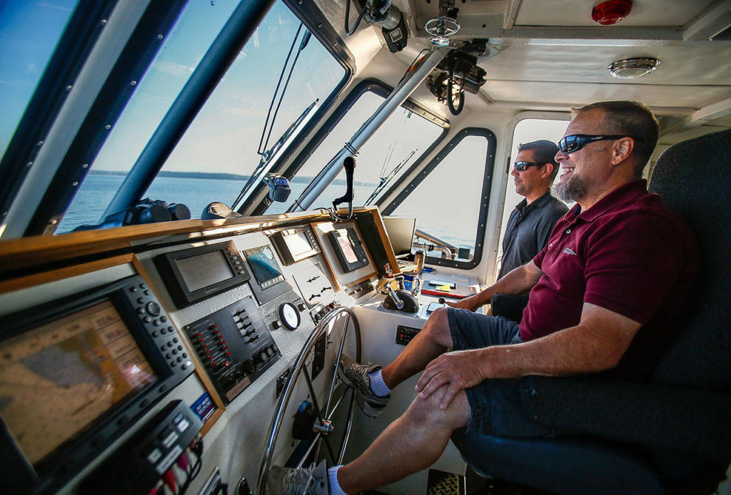 Captain Ray Brown (nearest) pilots the Hat Express early Thursday enroute to Hat Island as crew member Ryan Taisey, the first mate, watches for whales that have been spotted feeding nearby. (Dan Bates / The Herald)
