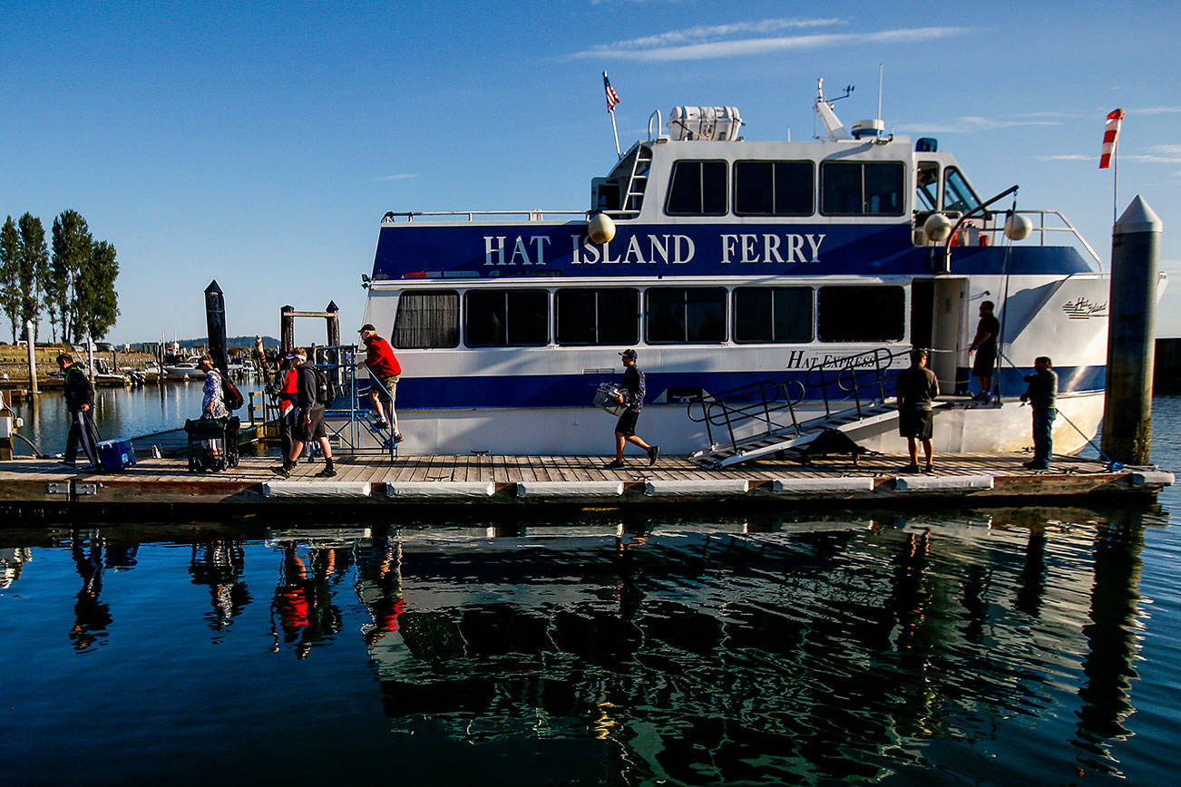 Arriving at Hat Island Marina early Thursday, islanders begin disembarking the Hat Island Ferry, which is called the “Hat Express.” At the top of the ramp stands Ray Brown, the captain. Below him on the dock are crew members Ryan Taisey, first mate (left) and Michael Jablinske. (Dan Bates / The Herald)