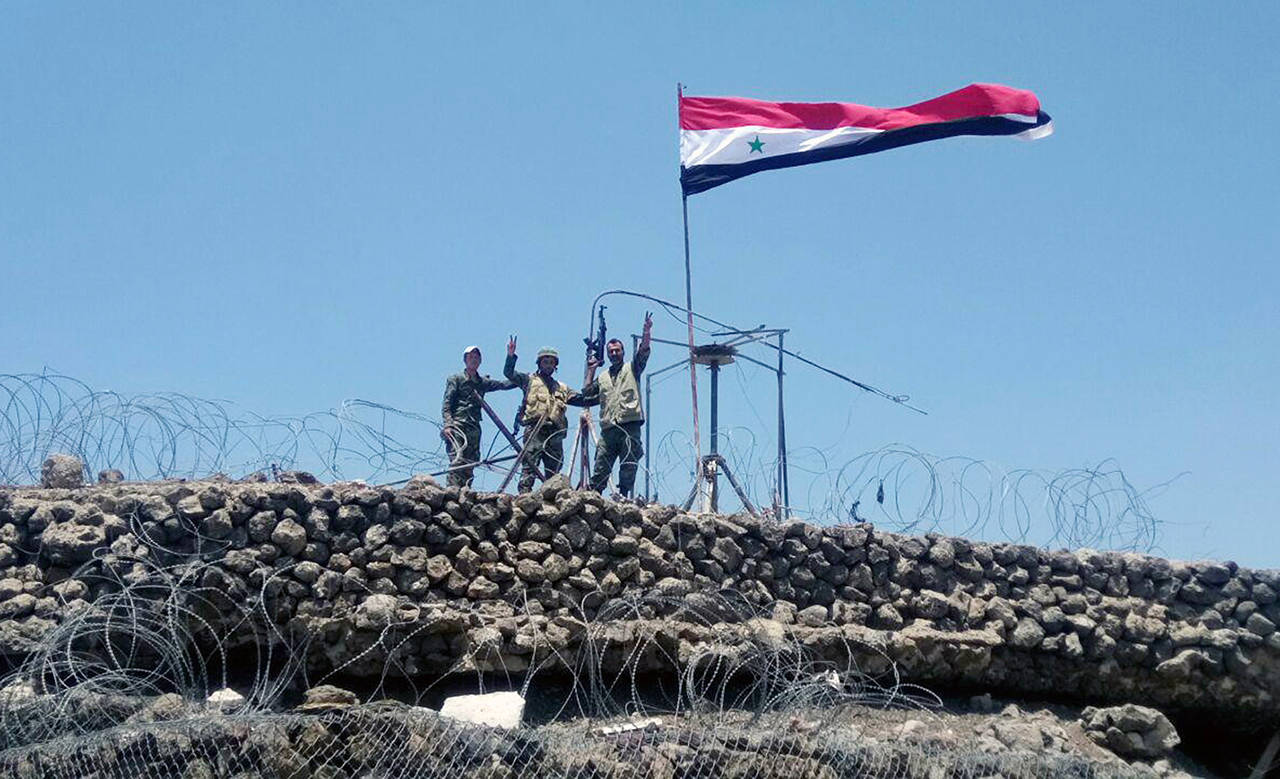 In this July 17 photo, Syrian troops flash the victory sign next to the Syrian flag in Tell al-Haara, the highest hill in the southwestern Daraa province, Syria. (SANA via AP, File)