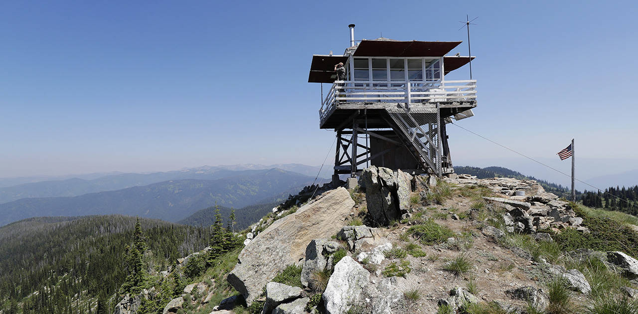 In this July 18 photo, Tom VandeWater stands at the railing of the Coolwater Fire Lookout and looks through his binoculars in the Nez Perce-Clearwater National Forests near Lowell, Idaho. VandeWater, from Canton, New York, has staffed the lookout each summer for many years for the U.S. Forest Service. (AP Photo/Ted S. Warren)