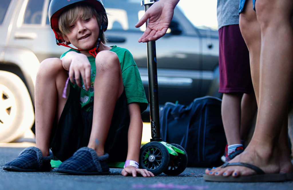 Quintin Hall rests for a moment on a scooter he was riding. Finding some purple Silly String on the driveway, he gives it to Lisa Marquart. (Dan Bates / The Herald)
