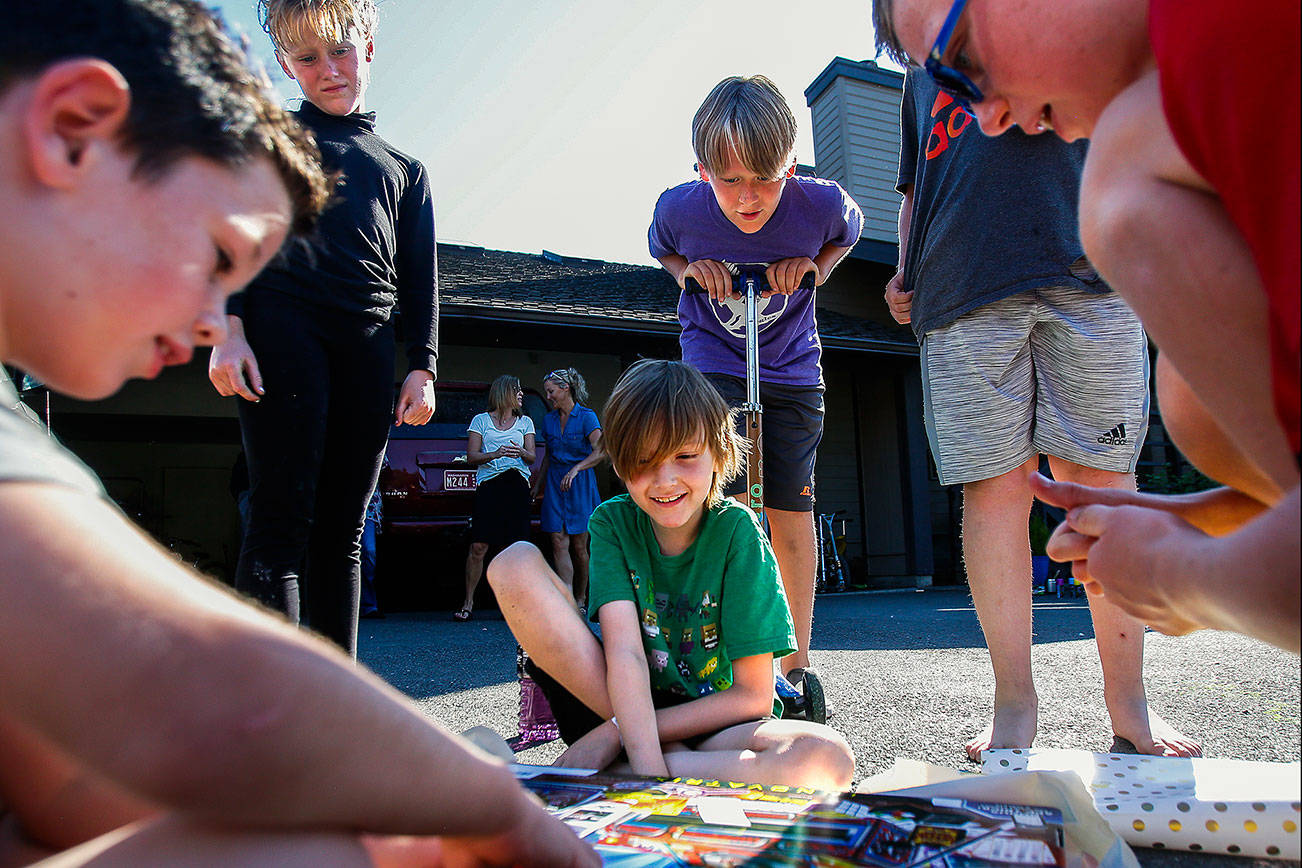 Quintin Hall, 8, (green T-shirt center) sits smiling as Kate Marquart, 8, (standing left), Alex Marquart, 11, (center) and Jonathan Marquart, 13, all watch Jack McGowan, 7, (left) and Max McGowan, 9, (right) peel open the wrapping on a going-away gift for Quintin. Along with his mom, Quintin is going home after an extended stay with the Marquart family while he had cancer treatment. (Dan Bates / The Herald)