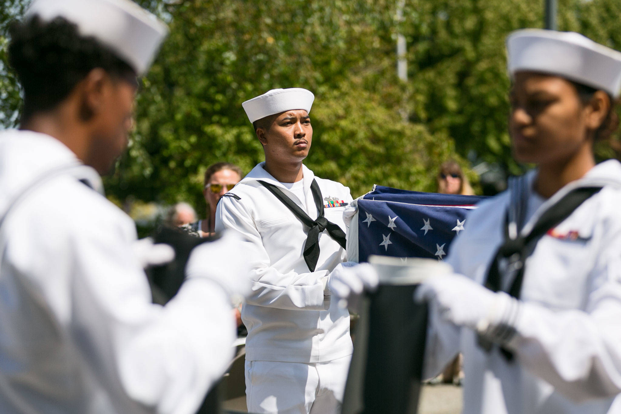 Naval personnel Allex Ok (center) holds the American flag as Stanley Parris (left) and Emele Clark finish folding the POW/MIA flag Friday afternoon during the decommissioning of the Snohomish County Courthouse Veteran Memorial in Everett. (Kevin Clark / The Herald)