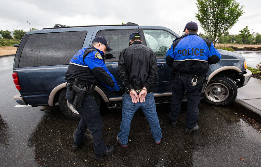 Monroe police officer Nathan Erdmann searches a suspect as Scott Kornish looks into a vehicle Wednesday, June 13, 2018, after the man was seen walking from a store with a possibly stolen item in the parking lot at Lowe’s. (Andy Bronson / The Herald)
