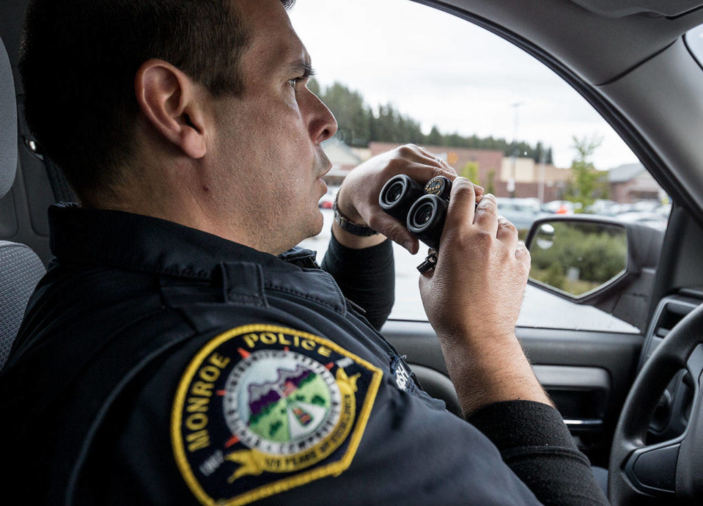 Looking for possible shoplifters, Monroe police officer Scott Kornish uses binoculars while staking out a spot in the parking lot of Lowe’s on Wednesday, June 13, 2018. (Andy Bronson / The Herald)
