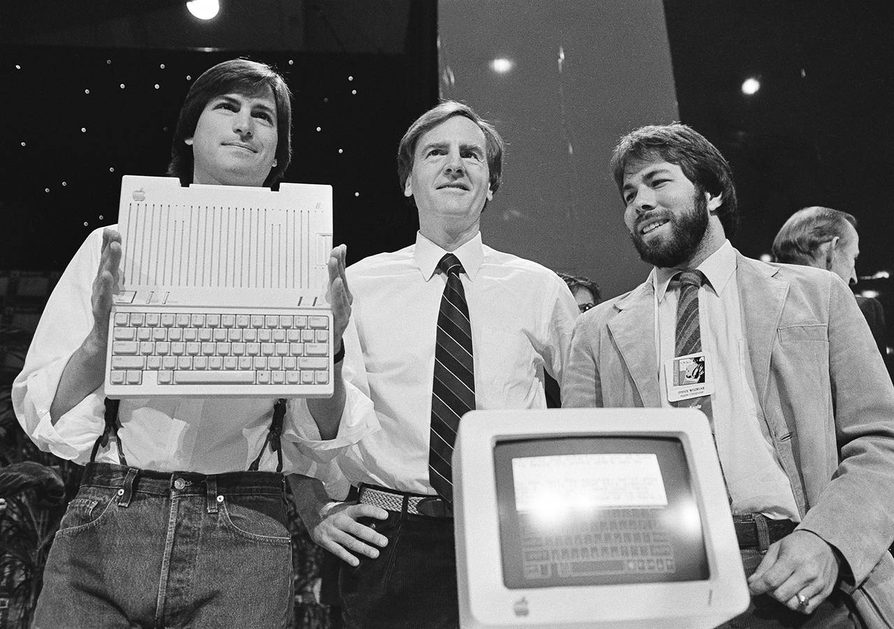 In this April 24, 1984 photo, Steve Jobs (left), chairman of Apple Computers, John Sculley (center), president and CEO, and Steve Wozniak, co-founder of Apple, unveil the new Apple IIc computer in San Francisco, California. (AP Photo/Sal Veder, File)