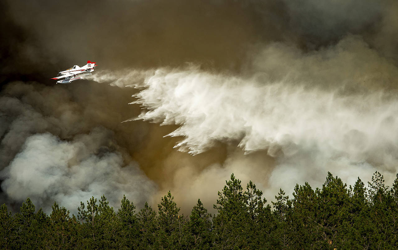 A firefighting aircraft makes a water drop on a wildfire approaching a house Tuesday in Spokane. (Colin Mulvany/The Spokesman-Review via AP)