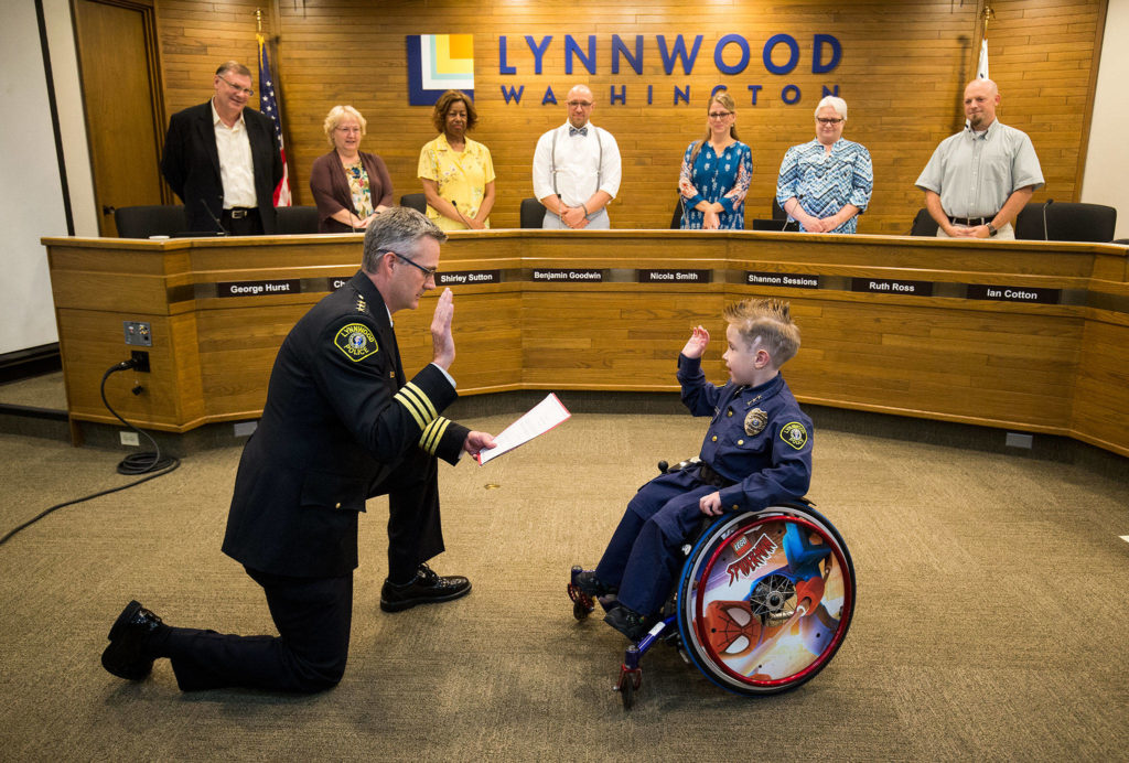 Chief for a Day Luca Keogh, 7, is sworn in as chief by Lynnwood Police Chief Tom Davis during a City Council meeting on Monday. It’s Lynnwood’s first time doing this. Keogh has been diagnosed with spina bifida, hydrocephalus, slit ventricle syndrome, chiari malformation and tethered cord syndrome. (Andy Bronson / The Herald) 
