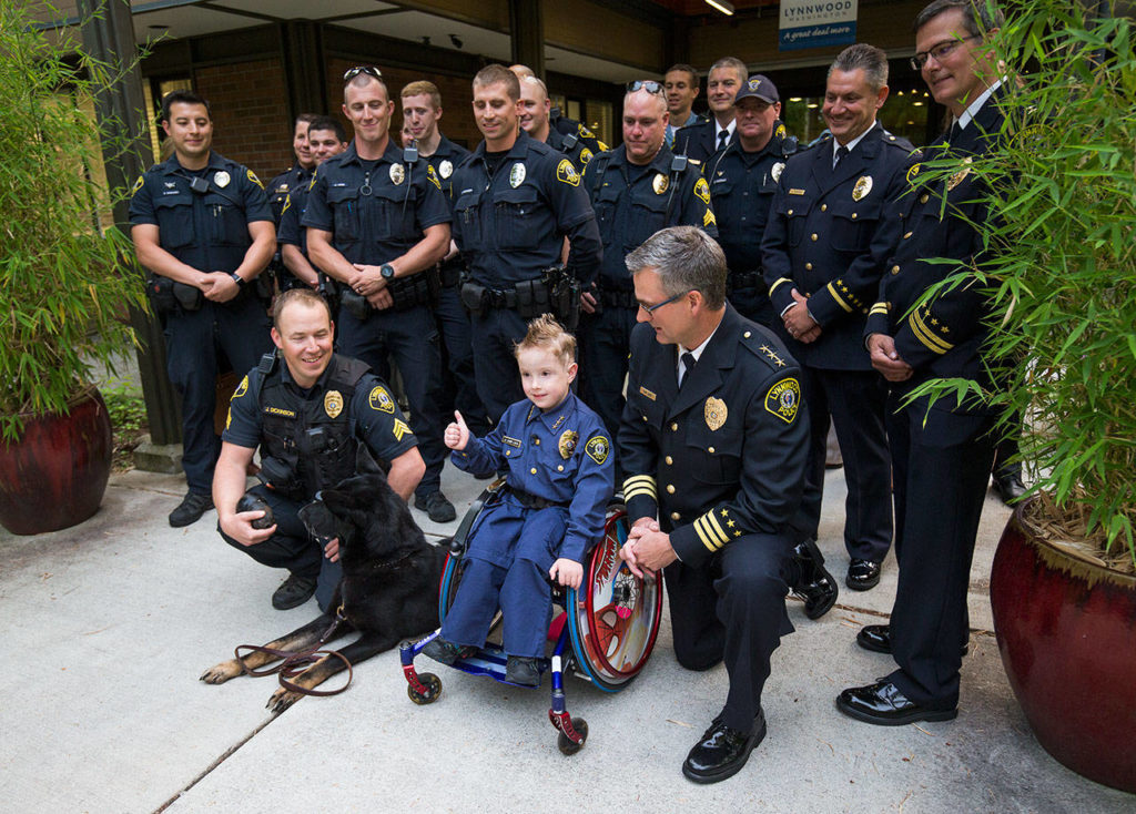 Chief for a Day Luca Keogh, 7, gives a thumbs-up during a photo op after he was sworn in as chief of Lynnwood police during a City Council meeting Monday. Keogh has been diagnosed with spina bifida, hydrocephalus, slit ventricle syndrome, chiari malformation, and tethered cord syndrome. (Andy Bronson / The Herald)
