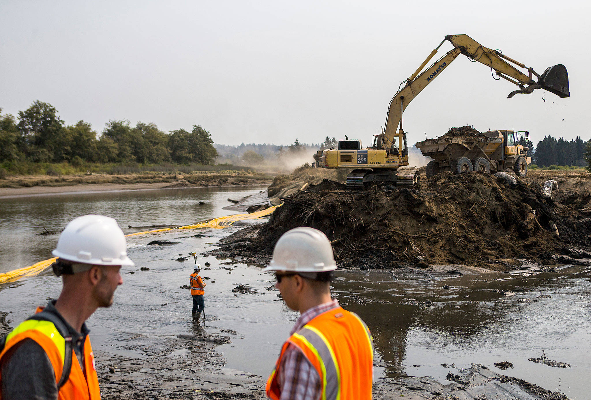 Snohomish County staff watch as an excavator breaches one of the dikes leading to the Snohomish River Estuary on Friday, Aug. 10, in Everett. (Olivia Vanni / The Herald)