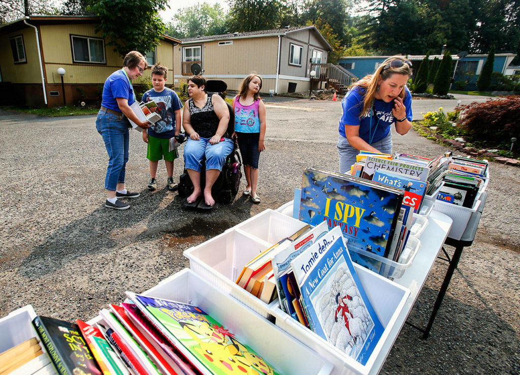 At Plantation mobile home park Tuesday, Book Cafe staff Kim Waltz (left) and Rebekah Fox (at right) select and show books to 8-year-old twins, Owen and Eva Wilkinson and their mom, Shannon. (Dan Bates / The Herald)
