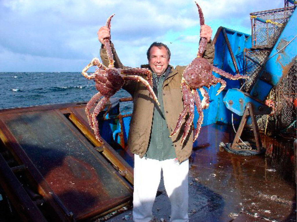 Dungeness Gear Works President Lance Nylander hoists two Alaskan blue king crabs on the deck of a ship. 
