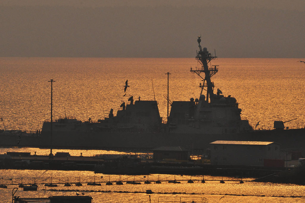 Naval Station Everett is silhouetted against the water’s reflection of the smoky evening sky Tuesday in Everett. (Sue Misao / The Herald) 
