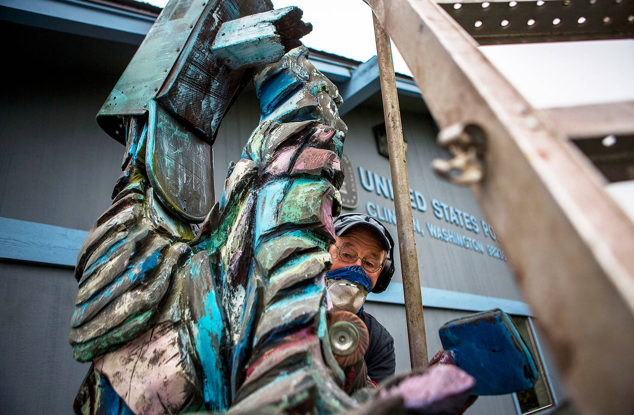Pat McVay works on touching up his woodcarving titled “Deluged” in front of the post office in Clinton. He is among 20 artists at this weekend’s Woodpalooza, a free show by the Whidbey Island Woodworkers Guild. (Olivia Vanni / The Herald)