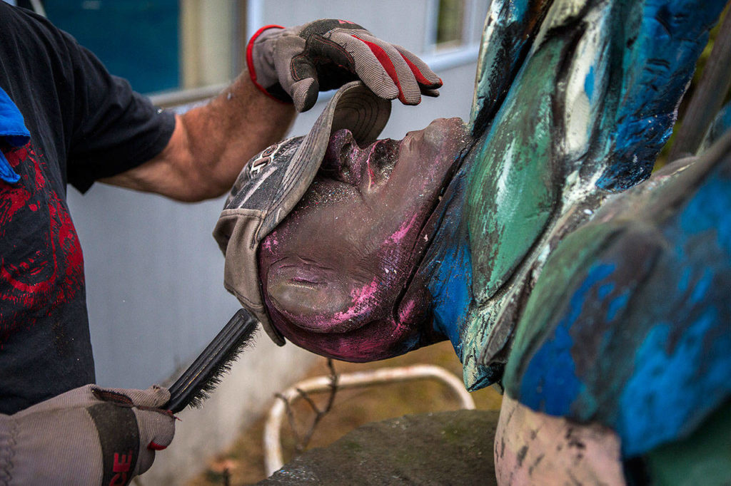 Pat McVay brushes off old paint from his woodcarving in Clinton. (Olivia Vanni / The Herald)
