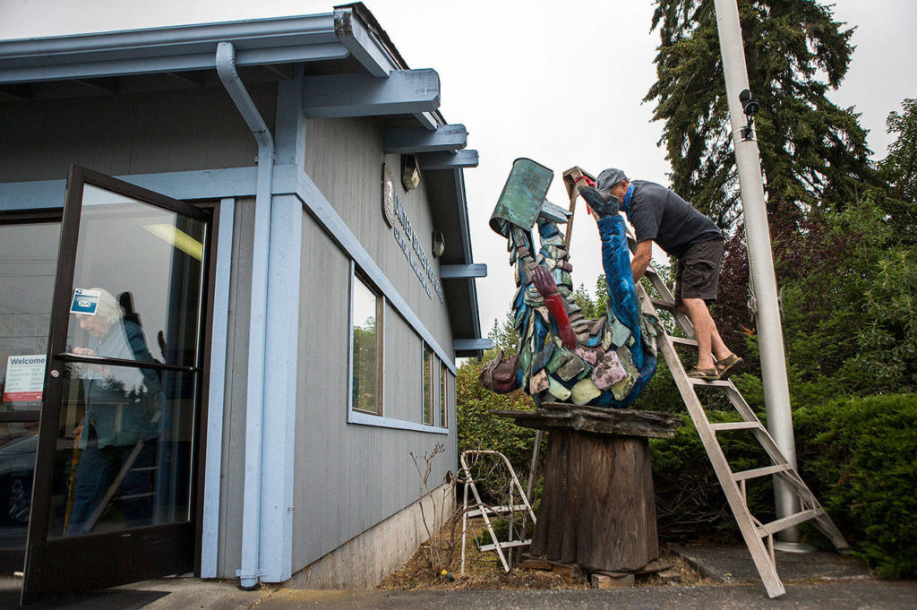 Pat McVay touches up his woodcarving in front of the post office in Clinton. (Olivia Vanni / The Herald)
