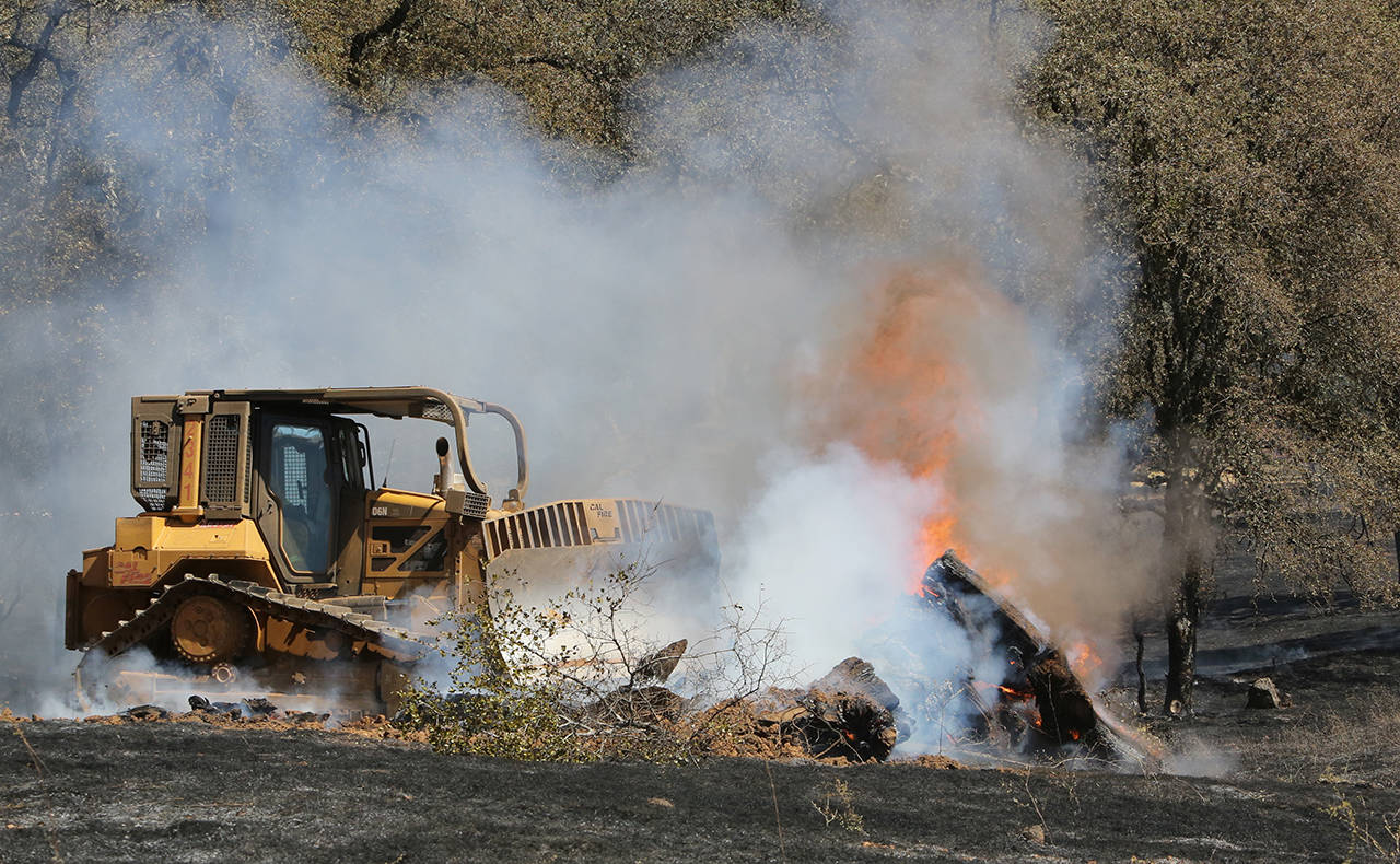 Cal Fire bulldozer 2341 pushes through a mound of burning vegetation due to a wildfire in Grass Valley, California, on Wednesday, Aug. 15. (Elias Funez/The Union via AP)