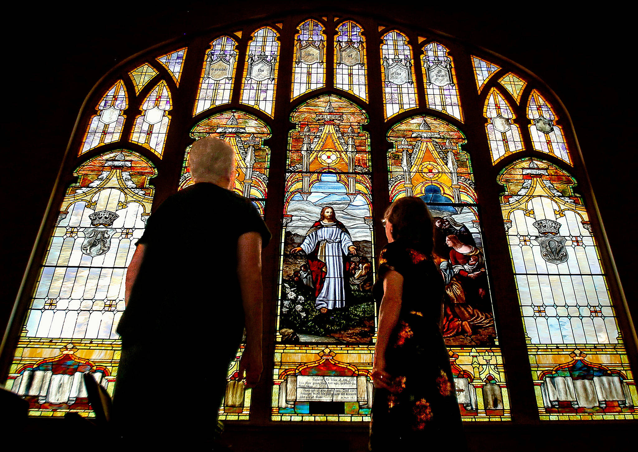 During the Everett Art Walk on Thursday, Laurie Povey Crawford (right) and Dottie Villesvik look at the large, east-facing stained-glass window with the interior lights turned down at First Presbyterian Church. The stained glass windows were created in 1910 by Povey Brothers Studio, where her great-grandfather, George Povey, worked with his brothers in Portland. (Dan Bates / The Herald)