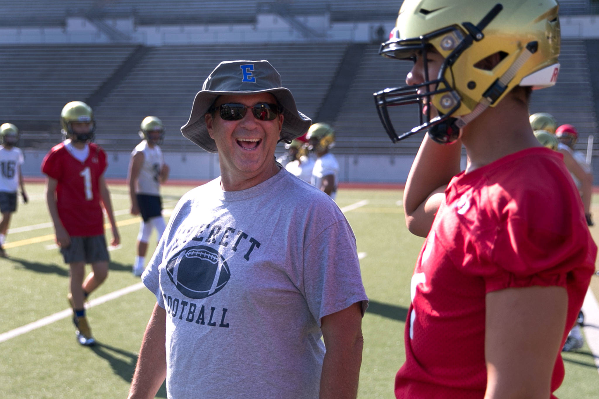 Everett coach David Coldiron (left) shares a laugh with quarterback Ethan Ollis during practice on Aug. 17, 2018, at Everett Memorial Stadium. (Kevin Clark / The Herald)