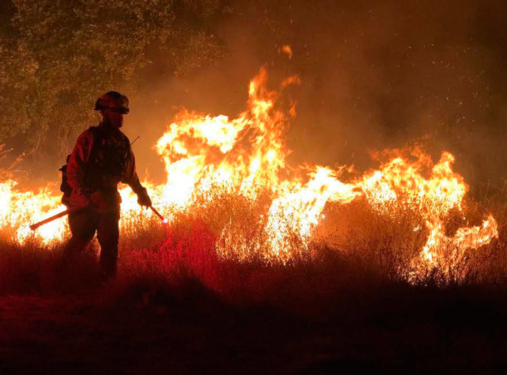 A firefighter walks near flames at the California wildfires. (Photo courtesy of Ernie Walters)
