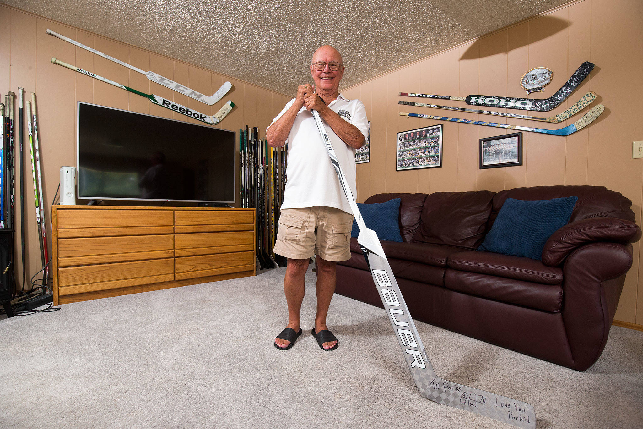 Parker Fowlds, who has been a Silvertips billet since the franchise began in 2003, stands among 54 hockey sticks on Aug. 17 in his Mukilteo living room. The house is filled with Silvertips memorabilia of players who have stayed with him over the years. (Andy Bronson / The Herald)