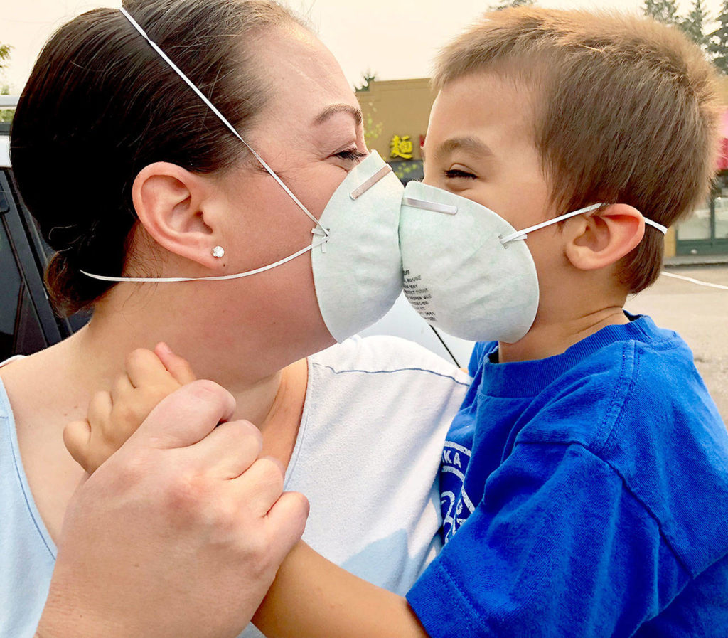 Jennifer Zahn, of Everett, bought a 10-pack of masks recommended for wildfire smoke. Her son, Jairus, 4, doesn’t seem to mind wearing one. “It tickles,” he said. Zahn said their family mostly stays inside and that they are thinking about leaving town for a couple of days to get away from the smoke — and the ash that covers her car. (Andrea Brown / The Herald)
