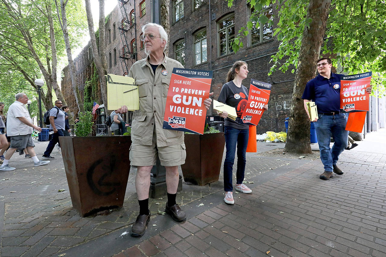 In this July 2 photo, Gus Webster (left), Pavi Chance (center) and Jordan Waits gather signatures for Initiative 1639 in Occidental Park in Seattle. (Greg Gilbert/The Seattle Times via AP, file)