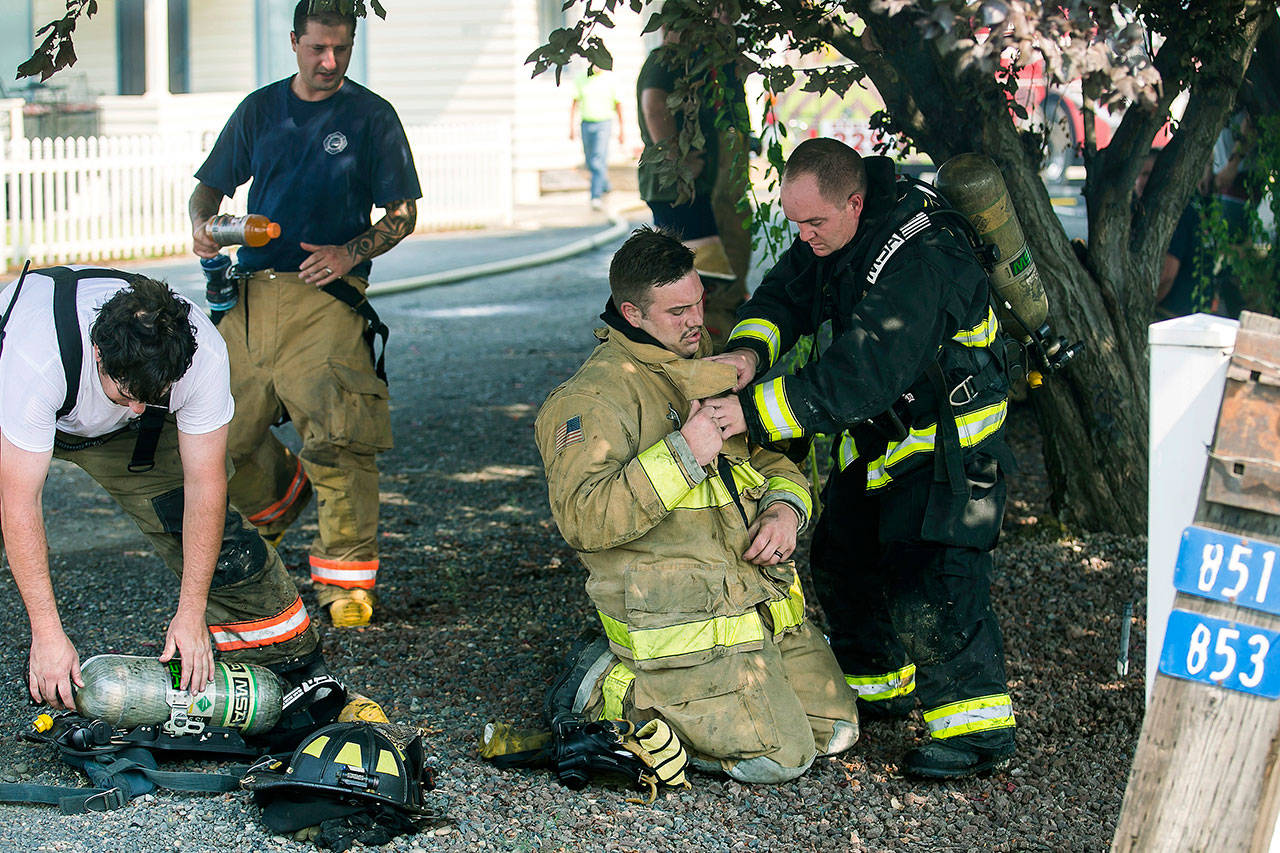 A Yakima firefighter assists a fellow firefighter after battling a structure fire Aug. 6 in Yakima. A rehab fire department vehicle is stocked with bottled water, sports drinks, food and other supplies needed to give firefighters relief from heat during fires. (Amanda Ray/Yakima Herald-Republic via AP)