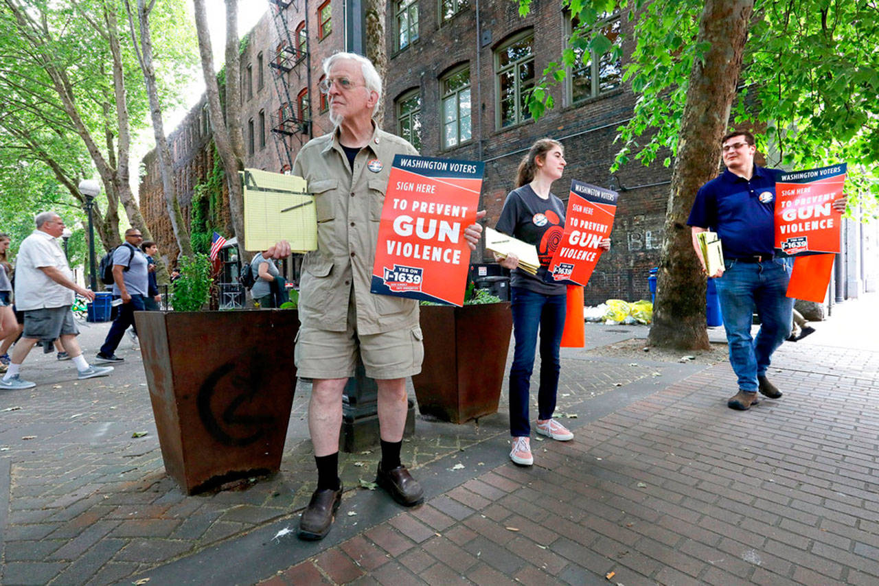 Gus Webster (left), Pavi Chance (center) and Jordan Waits gather signatures for Initiative 1639, at Occidental Park in Seattle, on July 2. The state Supreme Court on Friday overruled a lower court decision that would have kept the measure off the November ballot. (Greg Gilbert / The Seattle Times file photo)